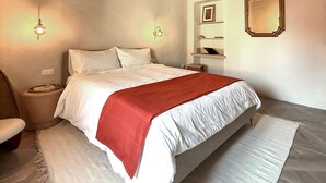 Een slaapkamer met een groot bed, houten balken in het plafond, een nachtkastje, een stoel en een spiegel aan de muur.