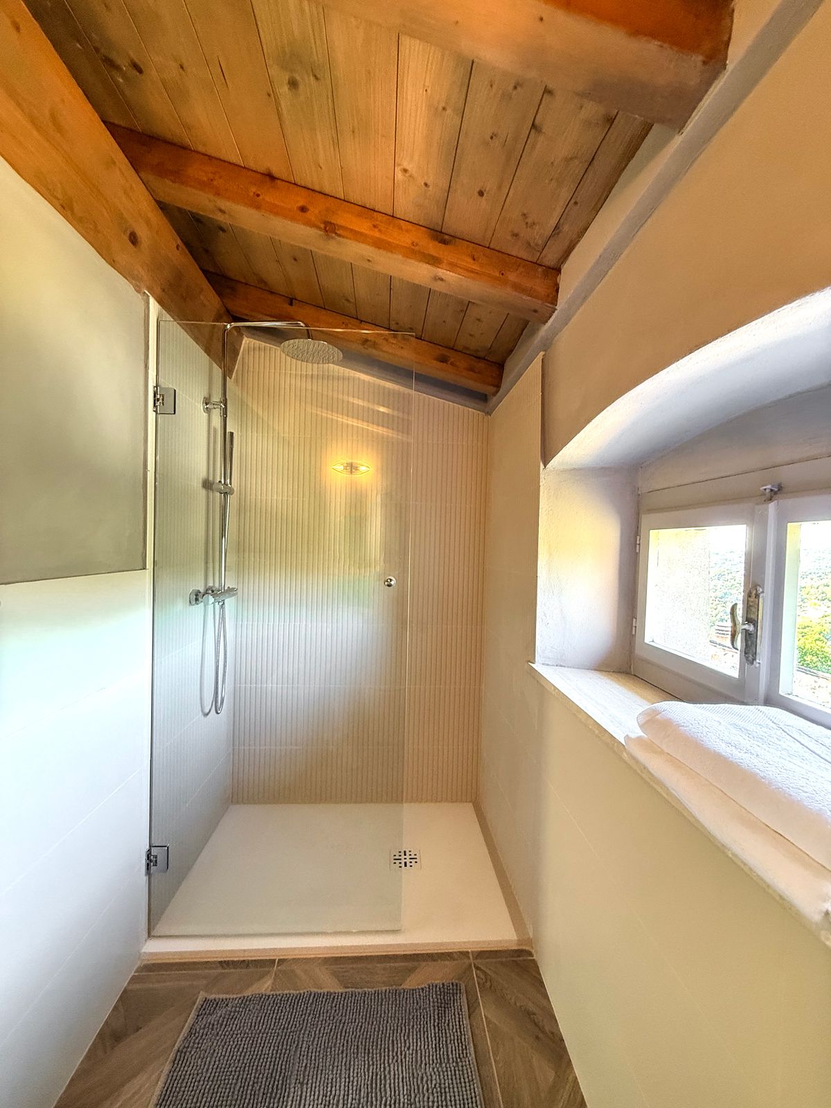Eine Dusche mit Glastür und einem Fenster darüber.