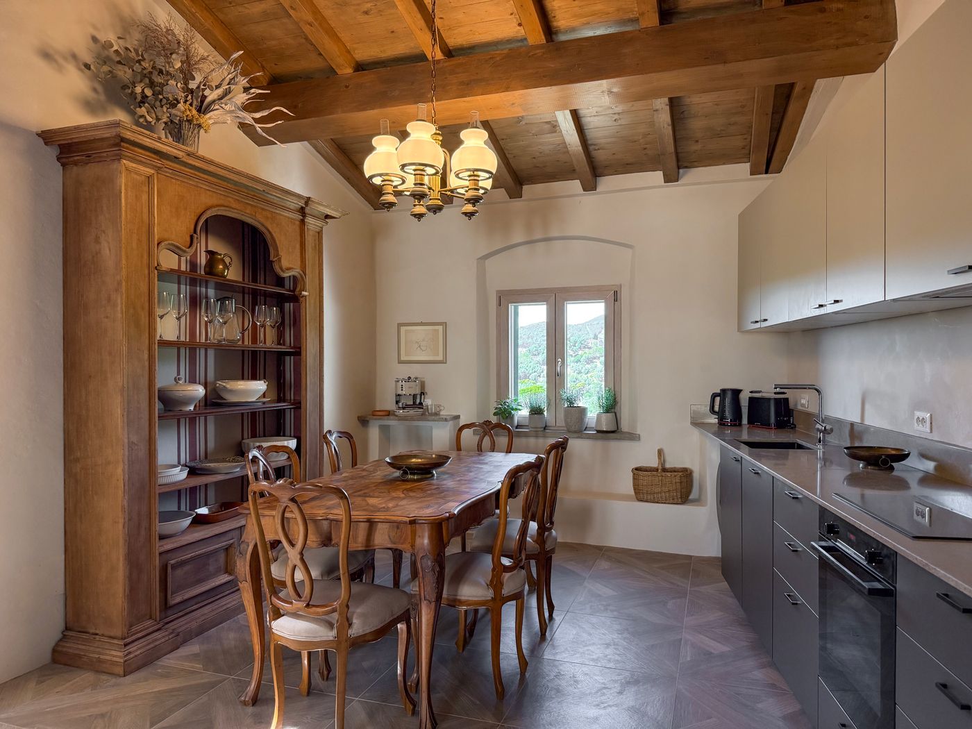 Ein Essbereich mit Holztisch und Stühlen, einem Schrank mit Gläsern und Blick ins Freie durch ein Fenster.