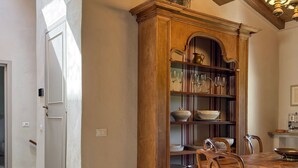 Een eetgedeelte met een houten tafel, stoelen en een ingebouwde boekenkast met glazen servies.
