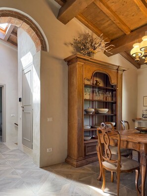 A dining area with a wooden table, chairs, and a built-in bookshelf with glassware. - Vrbo Property (Riparbella)