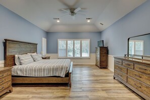 Een slaapkamer met een houten bed, een dressoir en een garderobe, een plafondventilator en ramen met zonwering.