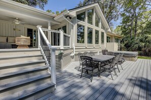 Een overdekt terras met een eettafel en stoelen, een trap naar een veranda, en een groot raam met uitzicht op een tuin.