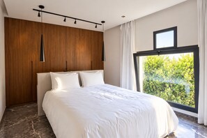 A modern bedroom with a large bed, wooden wardrobe, and a large window with a view of greenery. - Private Rooftop Pool—Large Apartment for 4 People (Marrakech)