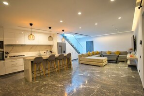A modern kitchen with a bar area, a staircase, and a living area with a sofa and cushions. - Private Rooftop Pool—Large Apartment for 4 People (Marrakech)