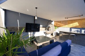 A modern outdoor living space with a flat-screen TV, a hanging chair, and a bar area. - Private Rooftop Pool—Large Apartment for 4 People (Marrakech)
