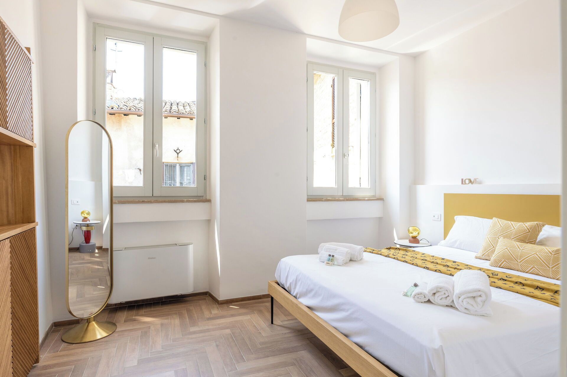 A hotel room with a bed, a bedside table, a mirror, and a window.