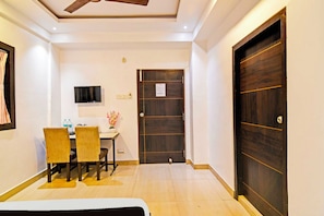 Habitación de hotel con cama, escritorio con televisor, puerta y una mesita con un jarrón de flores.