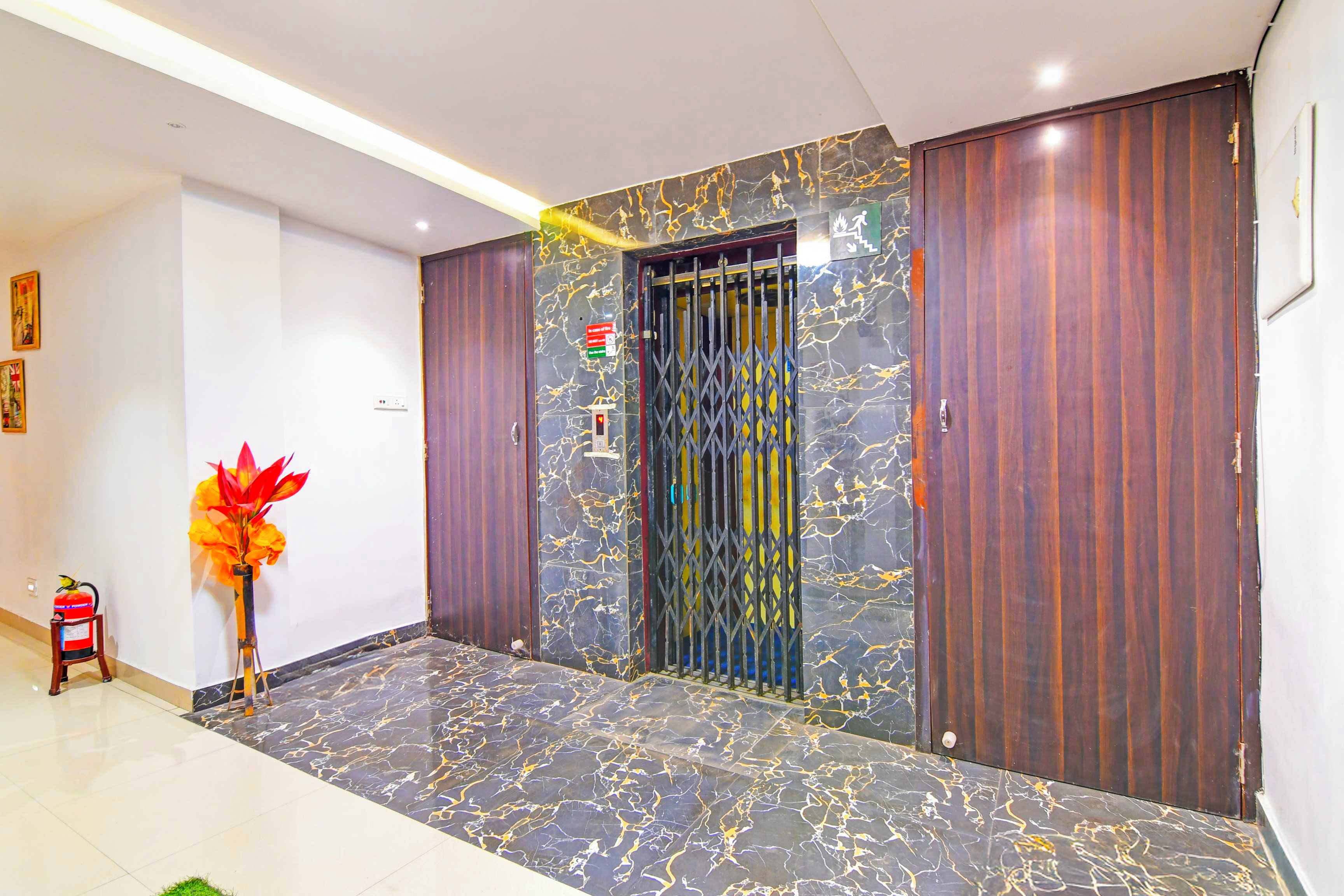 A hallway with a marble floor, a fire extinguisher, a vase with flowers, and a door with a security gate.