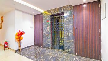 A hallway with a marble floor, a fire extinguisher, a vase with flowers, and a door with a security gate.