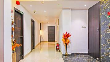 A hotel hallway with a marble floor, a fire extinguisher, and a decorative plant.