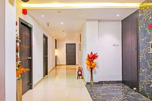 Un pasillo de hotel con piso de mármol, un extintor y una planta decorativa.