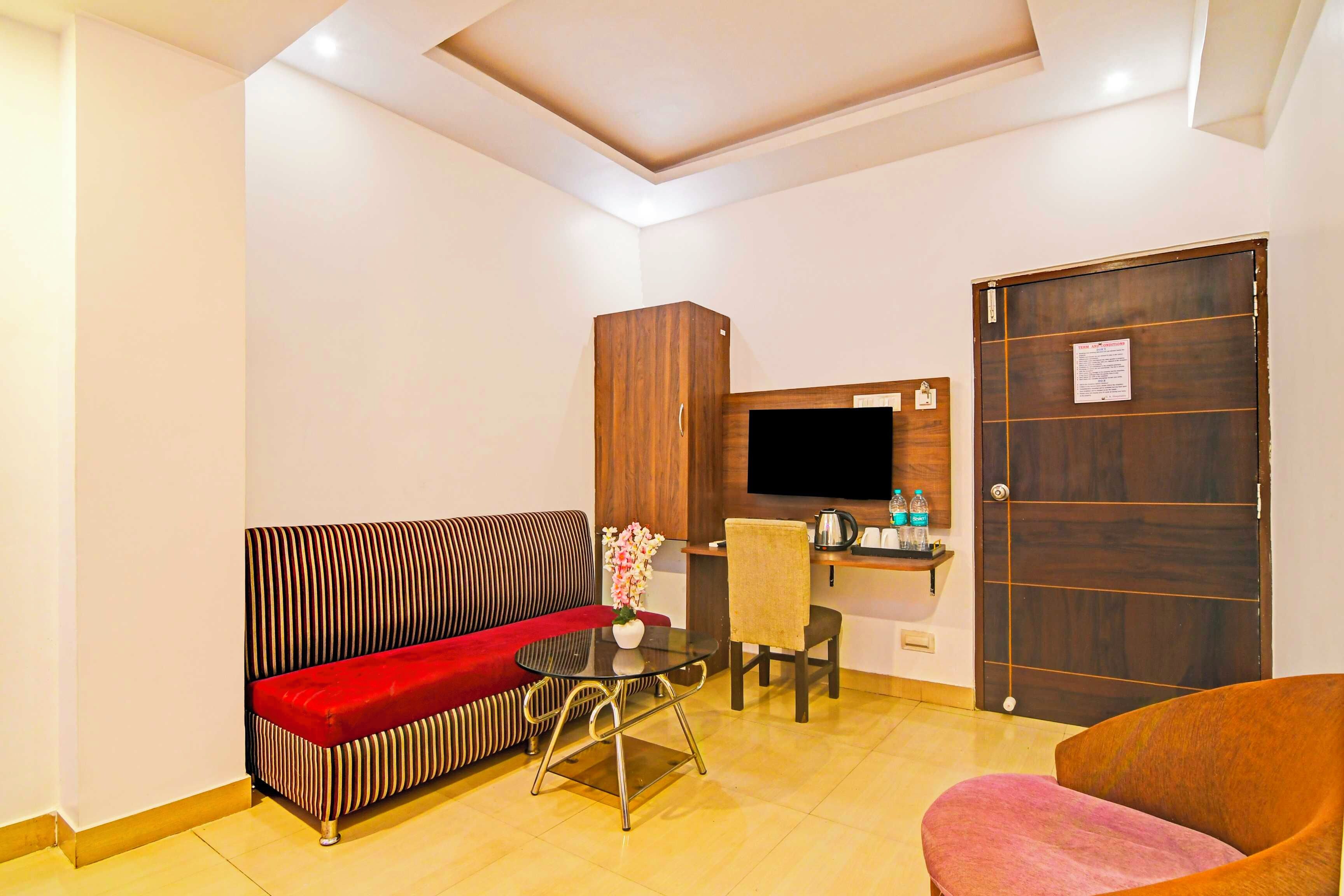 A hotel room with a sofa, a chair, a small table, a TV, and a wooden door.