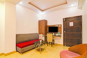 Une chambre d’hôtel avec un canapé, un fauteuil, une petite table, un téléviseur et une porte en bois.