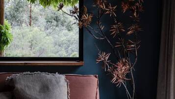 A room with a dark blue wall, a window with a view of greenery, a pink sofa with cushions, and a decorative plant.