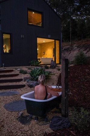 A person sitting in a bathtub outside a modern house with a visible interior.