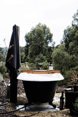 A bathtub with a wooden seat, surrounded by natural elements like trees and plants.