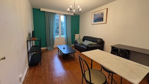 Una sala de estar amoblada con sofá, mesa de comedor, mesa de centro, televisor y ventana con cortinas.