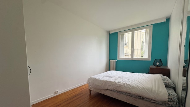 Un dormitorio con una cama individual, una ventana con persianas, una mesita de noche con lámpara y un radiador.