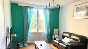 Una habitación con piso de madera, un sofá de cuero negro, una mesa de centro, un mueble de TV negro y una ventana con cortinas.