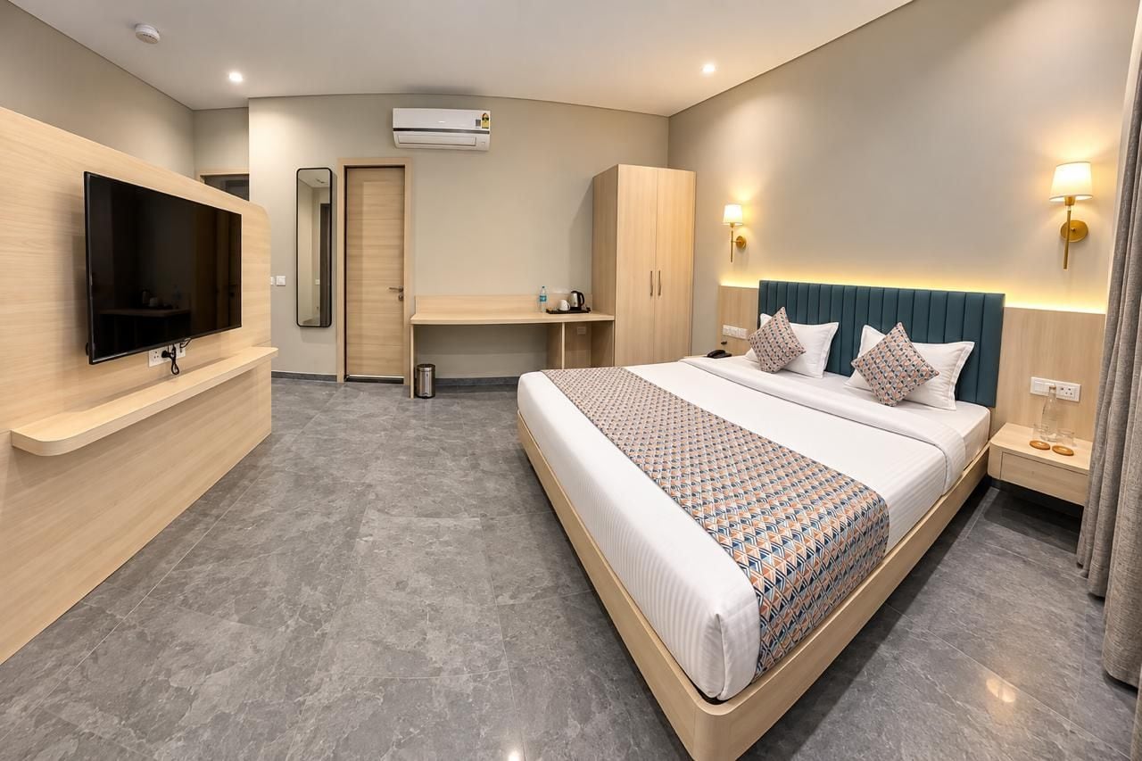 A modern hotel room with a bed, a TV, a desk, and a wardrobe.