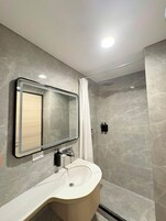 A modern bathroom with a curved sink, a mirror, and a shower enclosure.