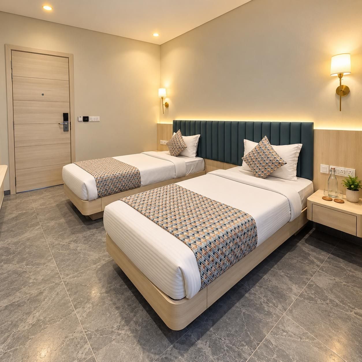 Habitación de hotel con dos camas, una puerta de madera, una mesita de noche con lámpara, y una lámpara fijada en la pared.