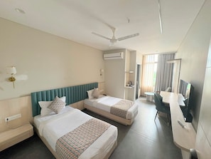 Quarto de hotel com duas camas, uma escrivaninha, uma televisão e ar condicionado.