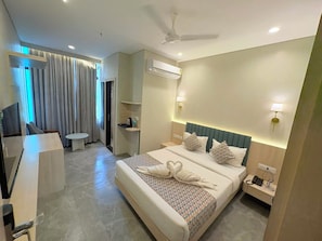 Quarto de hotel com cama, mesa de cabeceira, luminária e ventilador de teto.