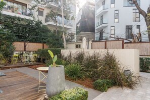 A courtyard with a wooden deck, outdoor seating, and a variety of plants. - Blueground Nahalat Bynamin City view (Tel Aviv-Yafo)