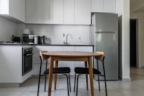 A modern kitchen with white cabinets, a stainless steel refrigerator, a microwave, and a stove. There is a wooden table with two chairs. - Blueground Nahalat Bynamin City view (Tel Aviv-Yafo)