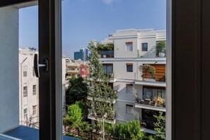 A view through a window of a modern apartment building with balconies, some with plants, and a clear sky. - Blueground Nahalat Bynamin City view (Tel Aviv-Yafo)