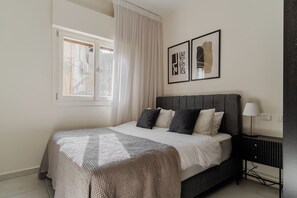 A bedroom with a bed, a window with curtains, a bedside table with a lamp, and two framed artworks on the wall. - Blueground Nahalat Bynamin City view (Tel Aviv-Yafo)
