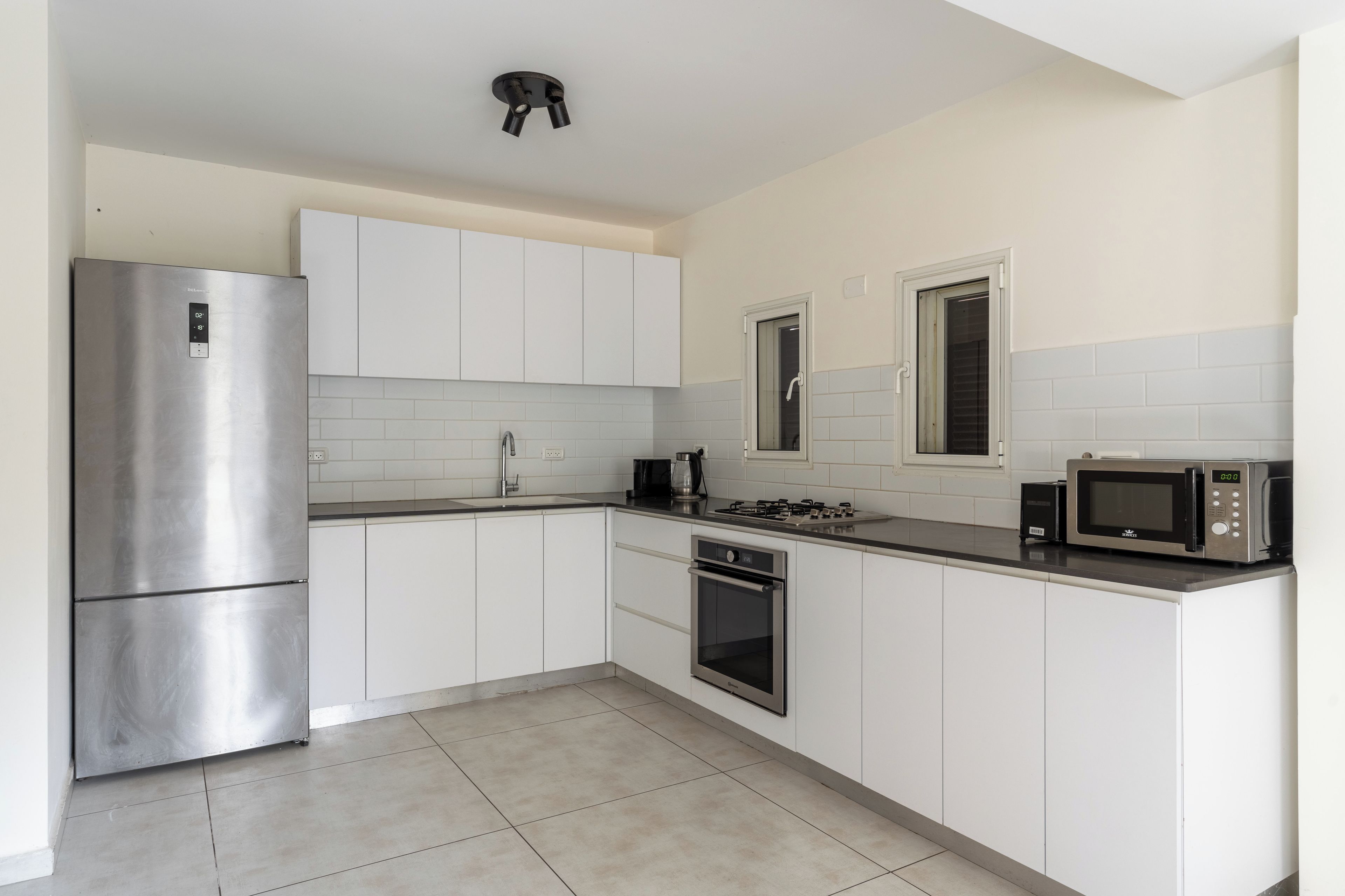 Een moderne keuken met witte kasten, roestvrijstalen apparatuur en een betegelde achterwand.