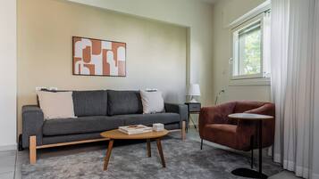 Una sala de estar moderna con un sofá gris, una mesa redonda y un sillón rojo. Hay una lámpara en una mesita auxiliar y una estantería llena de libros.