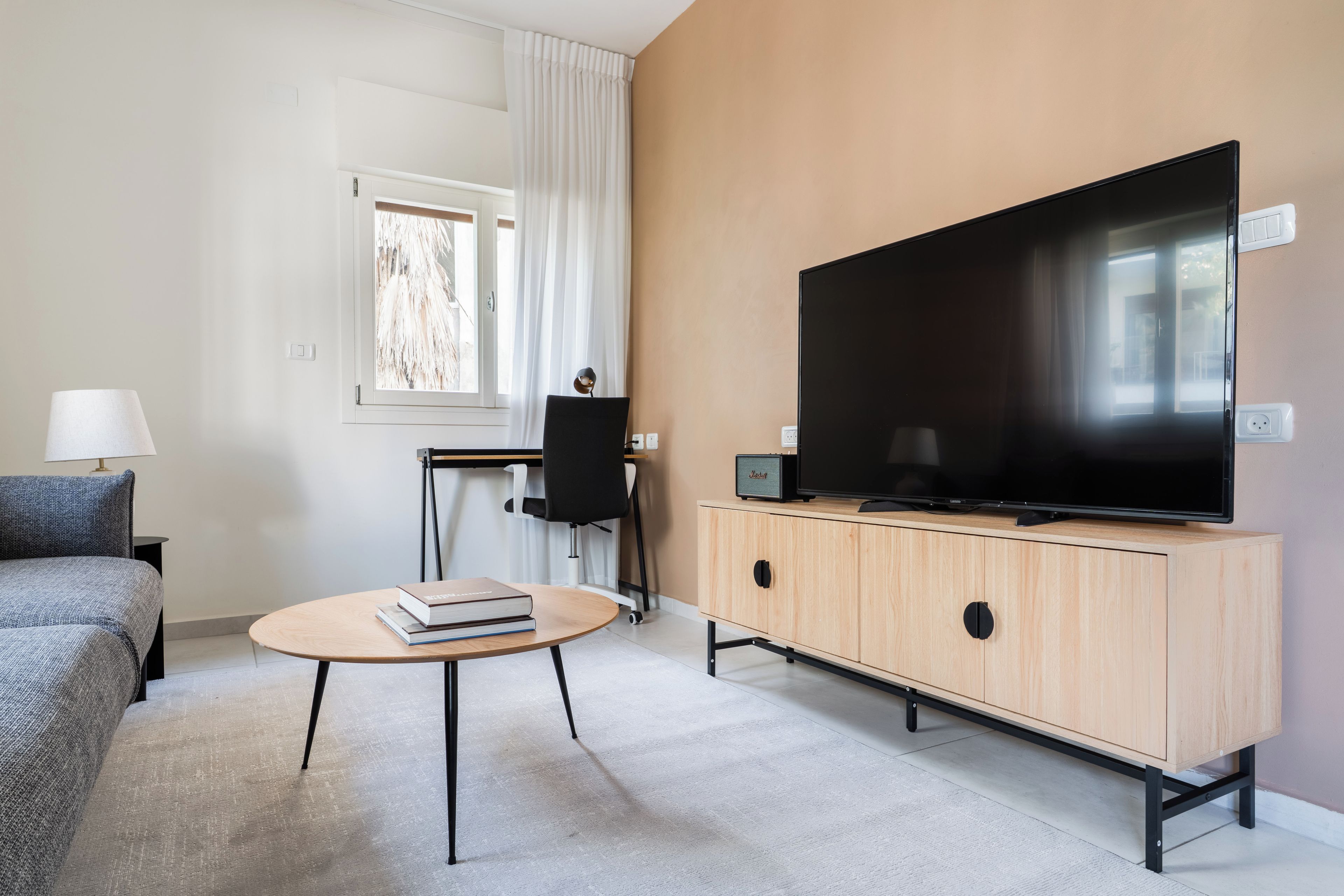 A modern living room with a flat-screen TV, a sofa, a small table with books, and a chair.