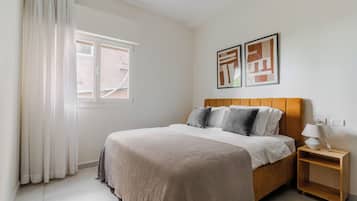 Ein Schlafzimmer mit einem Bett, einem Nachttisch, einem Fenster und zwei an der Wand hängenden Bildern.