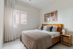 Un dormitorio con una cama, una mesita de noche, una ventana y dos cuadros en la pared.