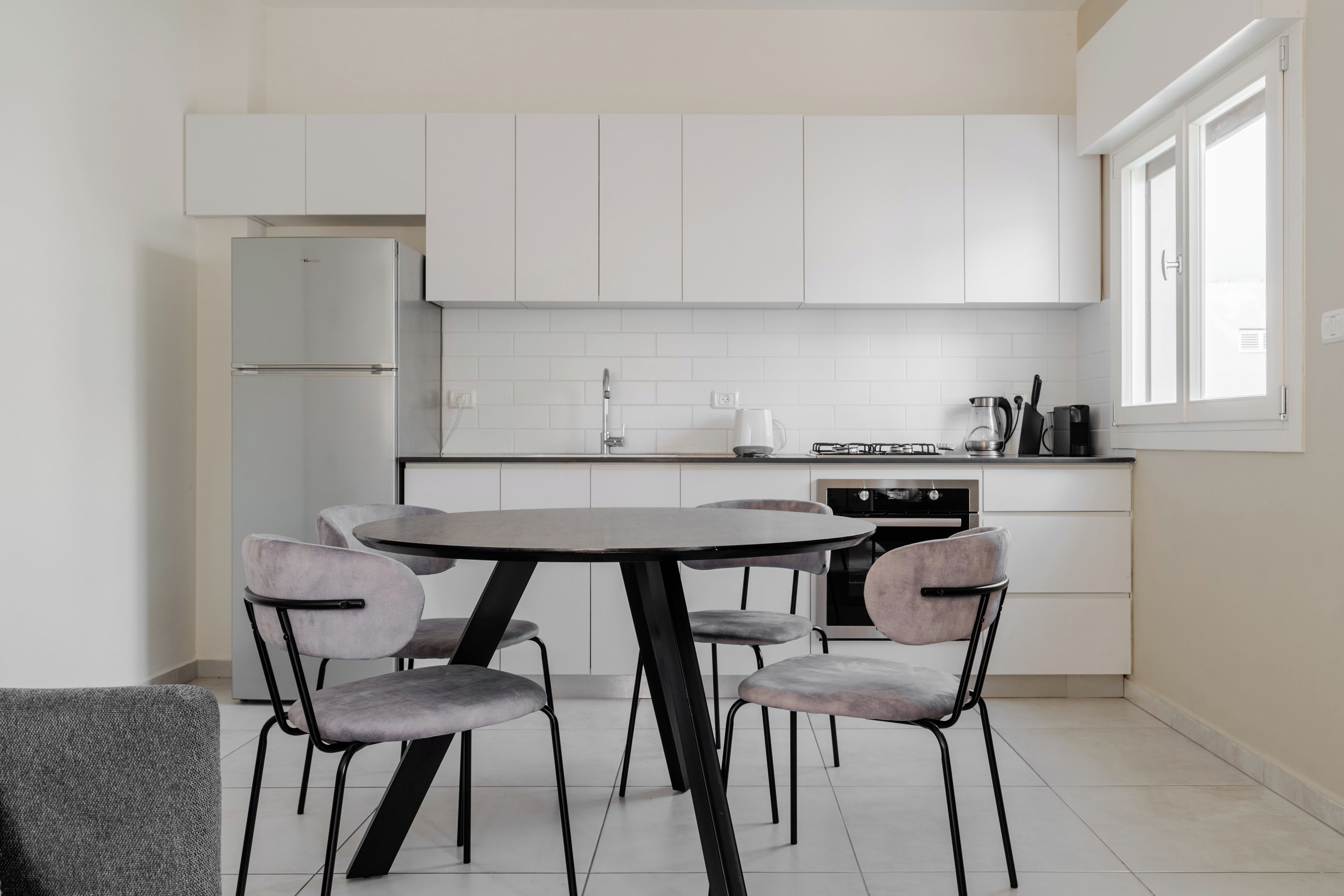 Una cocina moderna con armarios blancos, una mesa redonda y cuatro sillas.