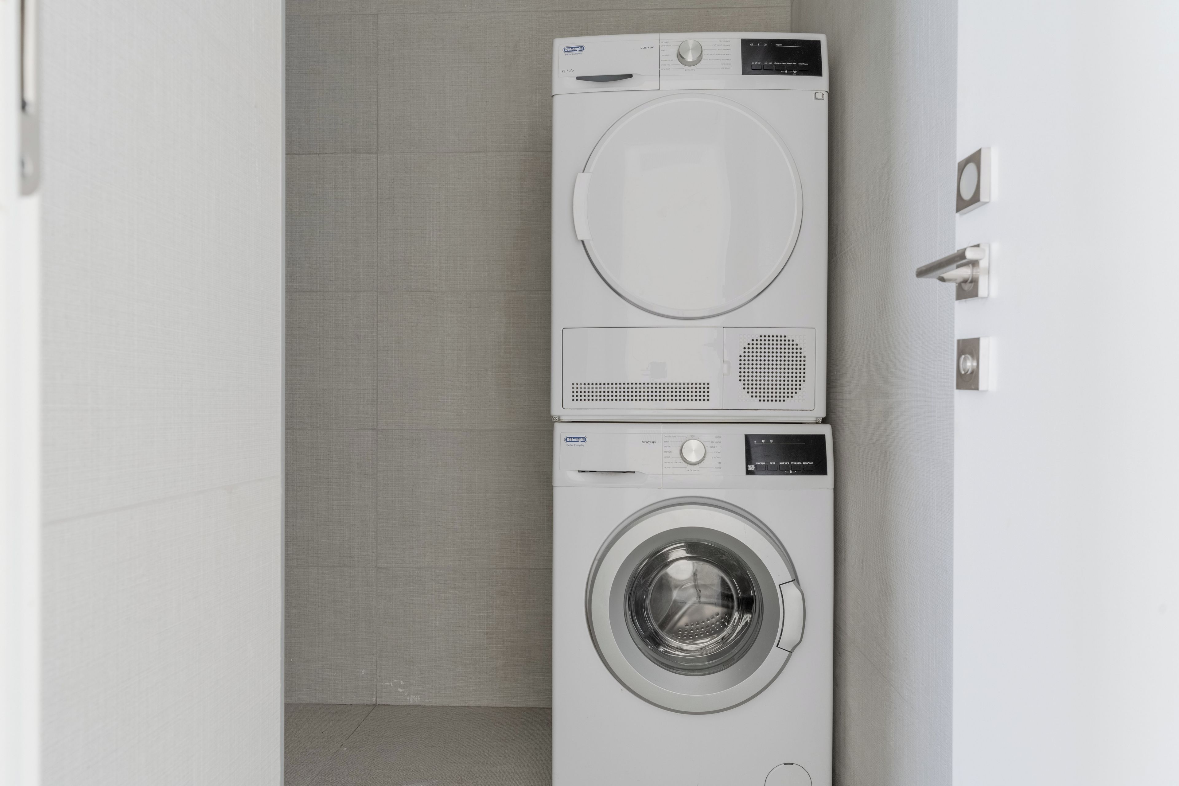 A compact, modern laundry room with a front-loading washer and dryer, a small control panel, and a tiled floor.