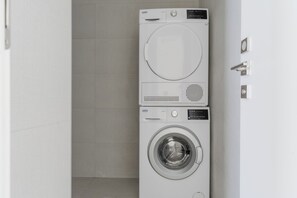 Un lavadero pequeño y moderno con lavadora y secadora de carga frontal, un panel de control discreto y piso de baldosas.