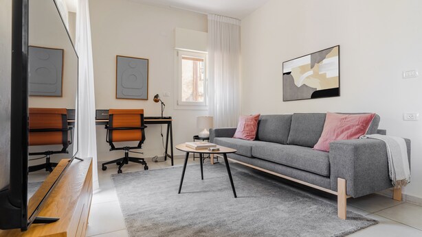 Una sala de estar moderna con un sofá gris, una mesita redonda y un escritorio con una silla.