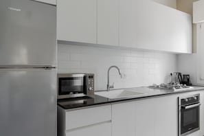 Uma cozinha moderna com geladeira de aço inoxidável, micro-ondas embutido, fogão a gás e pia.