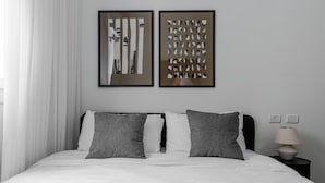 Una cama bien hecha con dos almohadas, una mesita de noche con una lámpara y dos cuadros abstractos enmarcados en la pared.
