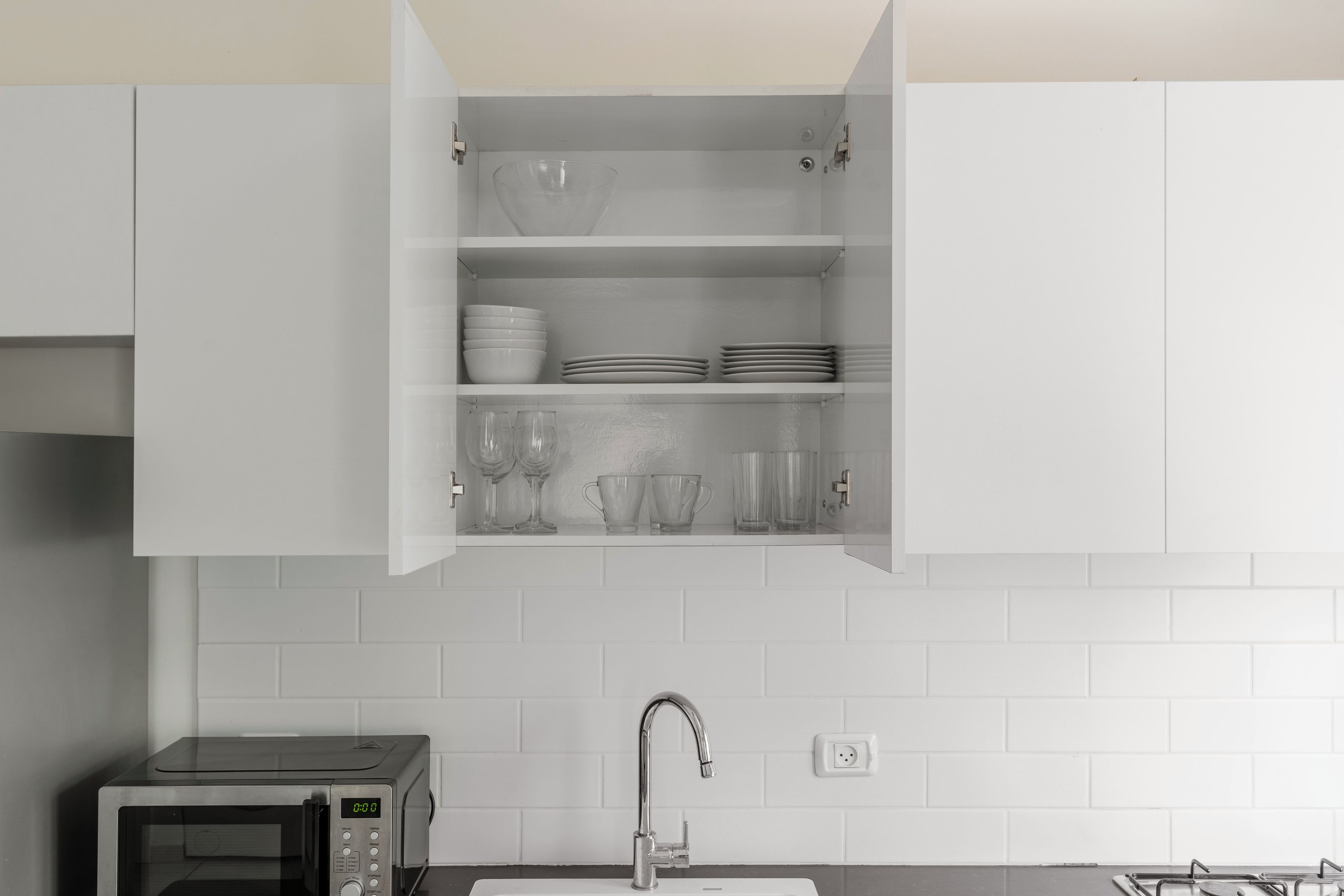 Eine Küche mit einer Mikrowelle, einem Spülbecken und einem Schrank mit Geschirr und Gläsern.