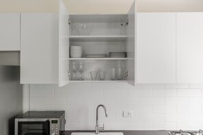 Una cocina con microondas, un lavamanos y un armario con vajilla y vasos.