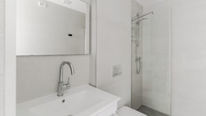 Un baño moderno con un lavamanos blanco, un espejo y una ducha con mampara de vidrio.