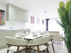A modern dining area with a table set for four, white chairs, and a kitchen in the background. - Modern 3-Bed Wembley Home, Minutes from Wembley Stadium (Wembley)
