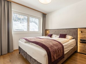 A bedroom with a large bed, a window with a view of a snowy landscape, and a wooden headboard. - Holiday Apartment With 1 Bedroom (Rauris)