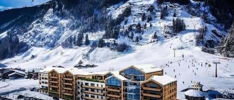 A hotel with multiple floors, a ski slope in the background, and a parking area.